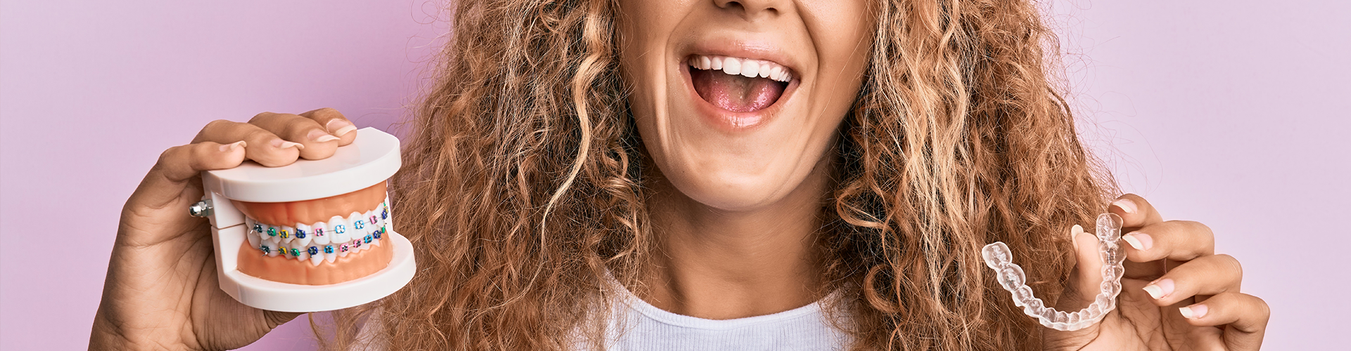 womain holding clear aligner in one hand and mouth model with braces in the other