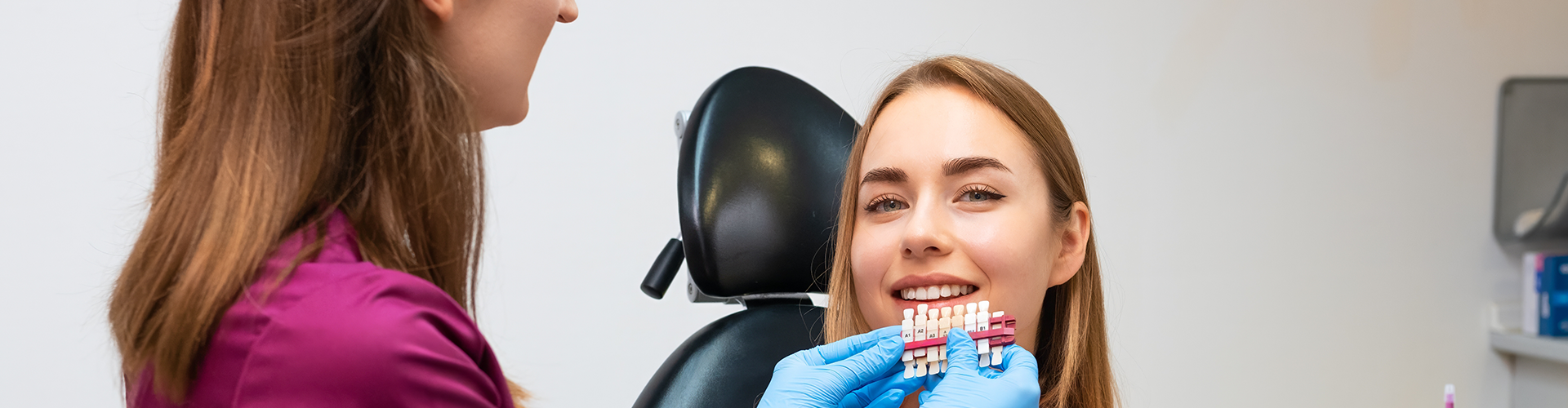 dentist holding tooth shade-matching tool against patient's smile