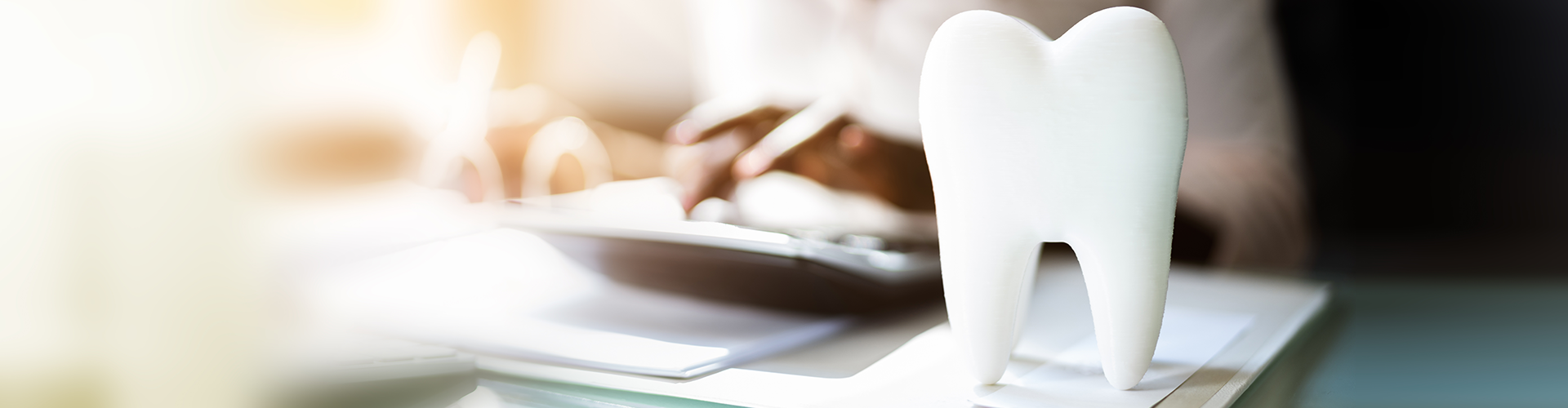 large tooth model sitting on paperwork while person types on calculator in background