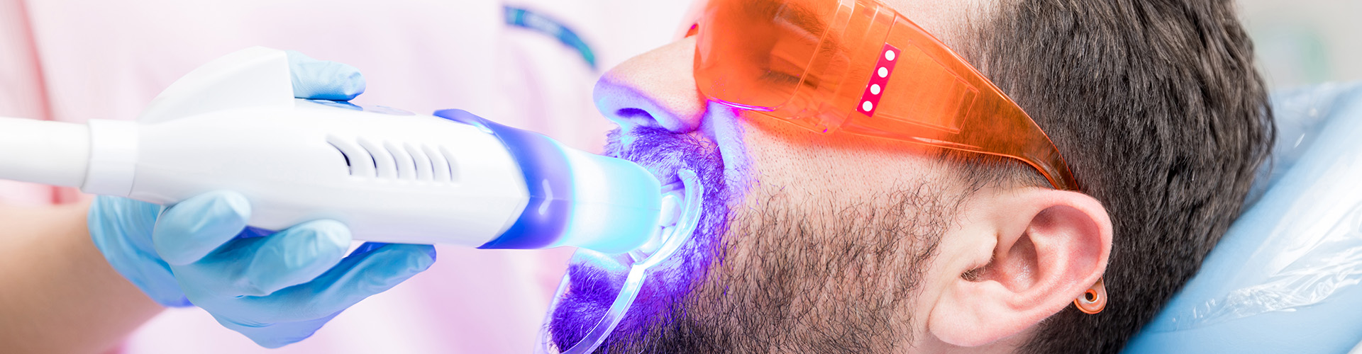 A man receiving a dental cleaning with ultraviolet light.