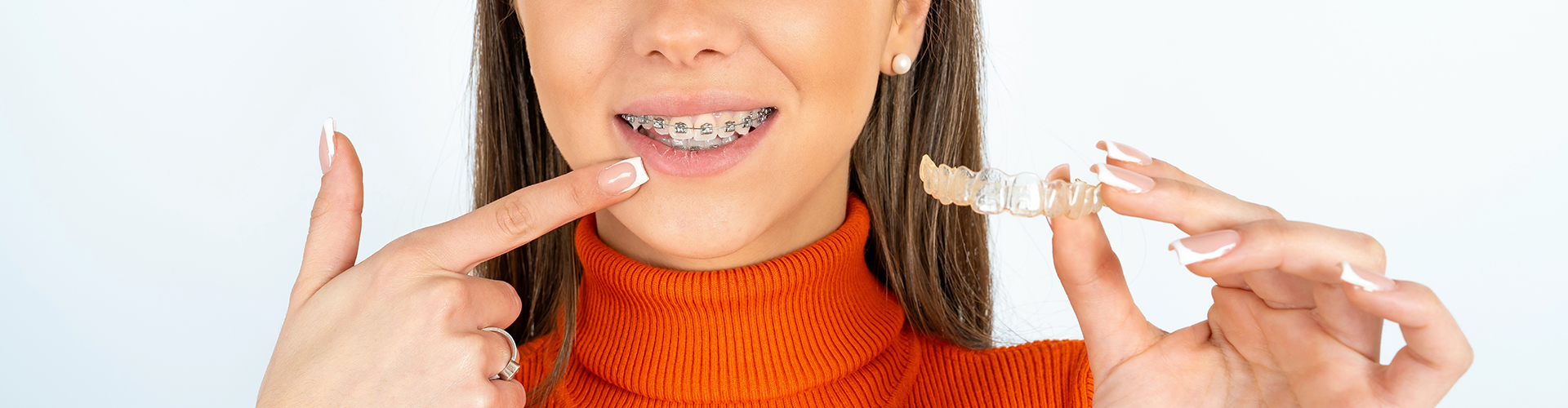 woman holding clear aligner and pointing at her braces