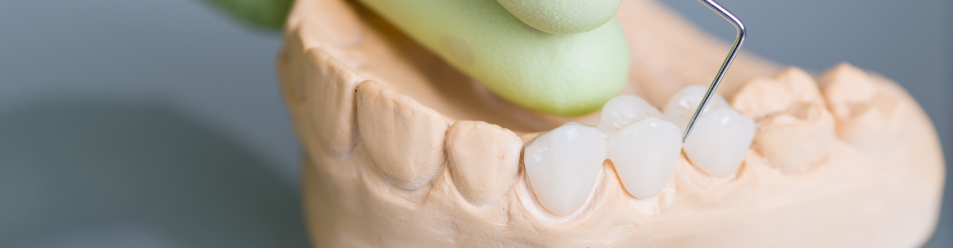 gloved hand using dental tool on dental bridge on mandible model