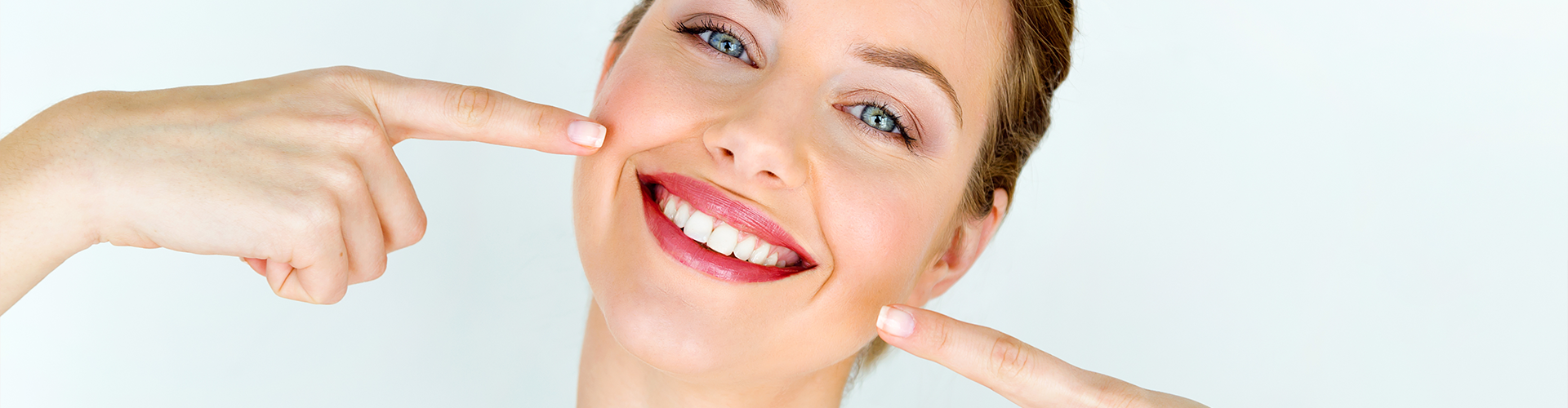 A woman pointing to her smile with both hands.