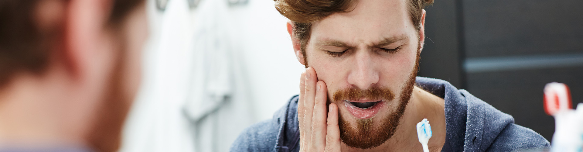 Man holding cheek in pain while brushing teeth.