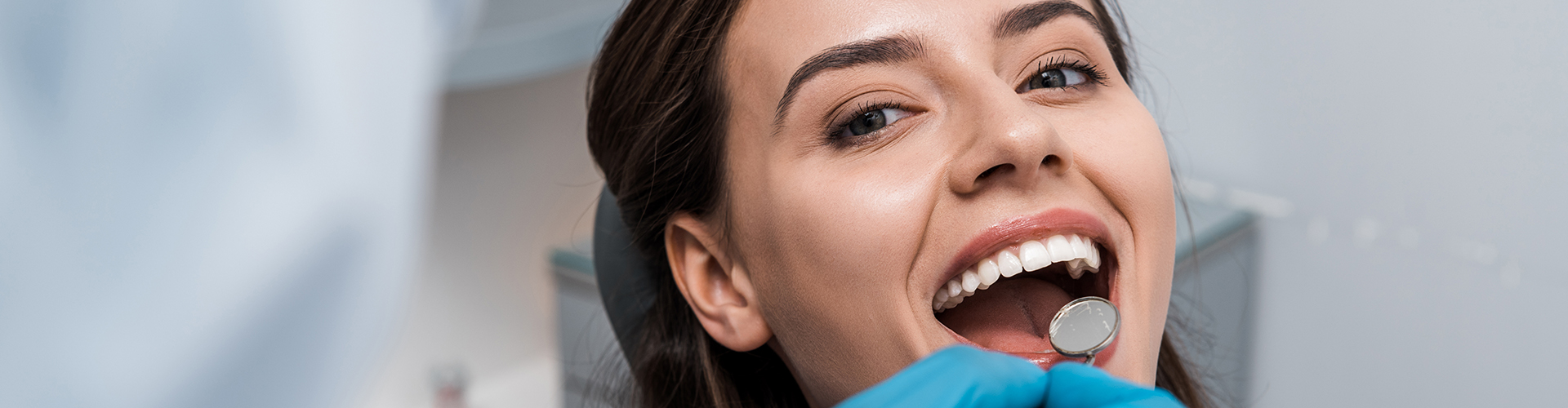 A woman with her mouth open, smiling while being examined with a dental mirror.